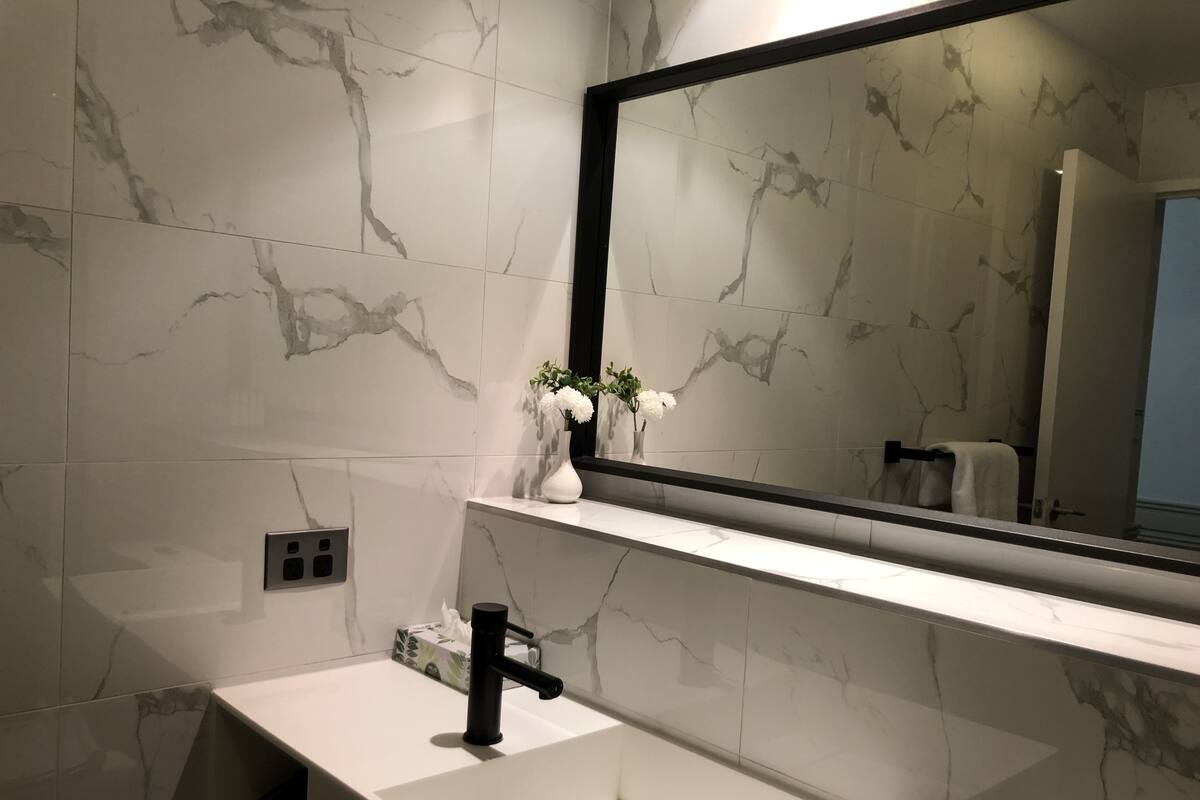 Un baño moderno con un salpicadero de mármol, un lavabo blanco y un grifo negro.