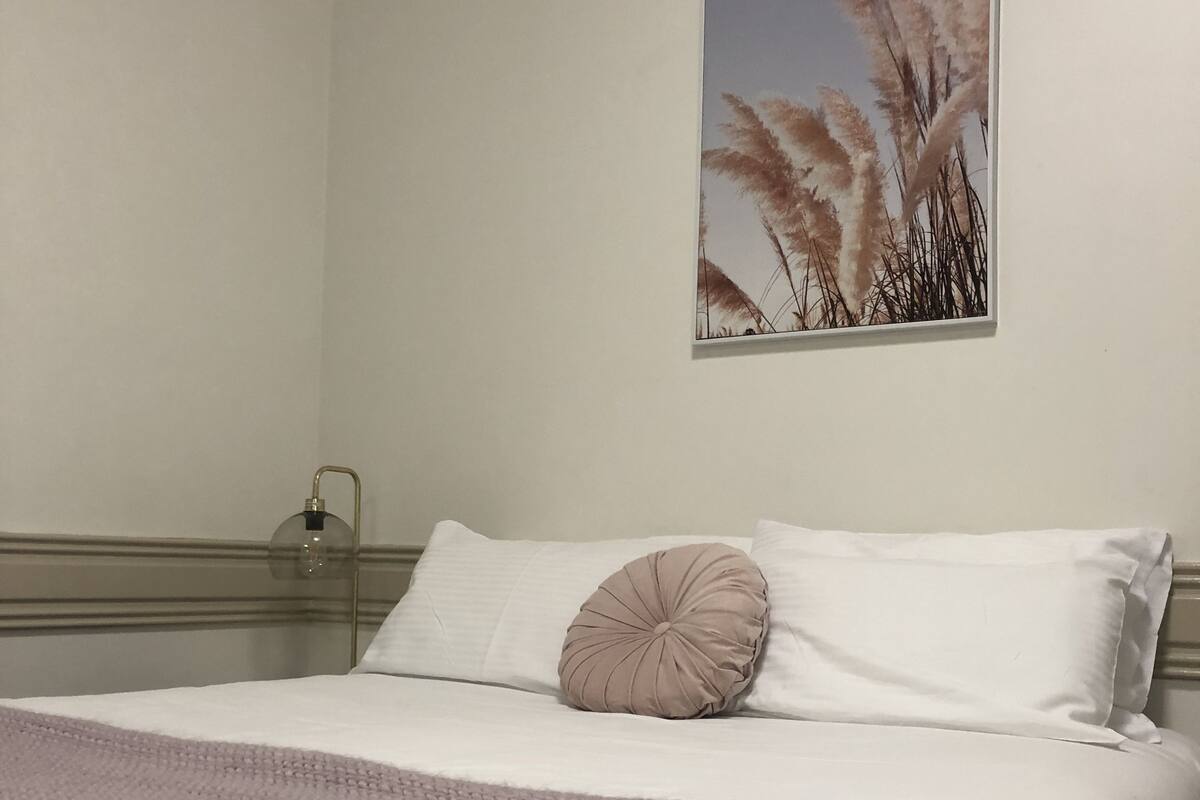 Una cama bien hecha con cabecera blanca, almohada color beige y manta tejida.