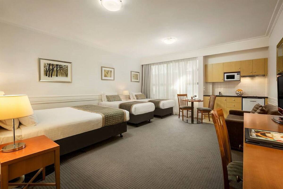 Habitación de hotel con dos camas, un escritorio, una silla, una kitchenette pequeña y un televisor.