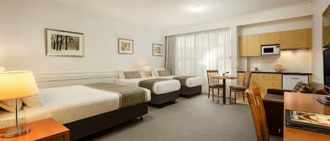 A hotel room with two beds, a desk, a chair, a small kitchenette, and a TV.