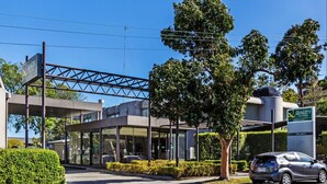 Entrada de hotel moderna con un toldo, un automóvil estacionado frente a ella y un letrero que indica habitaciones disponibles.