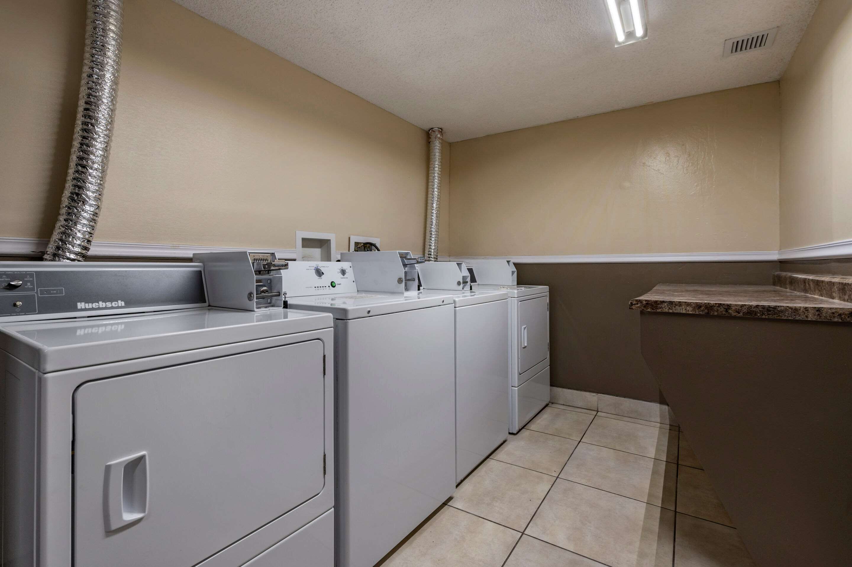 A laundry room with a front-loading Huebsch washer and dryer, a small sink, and a vent pipe.