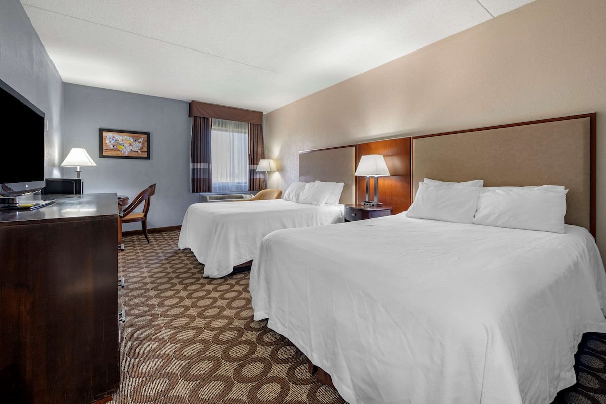 A hotel room with two beds, a desk, a TV, and a patterned carpet.
