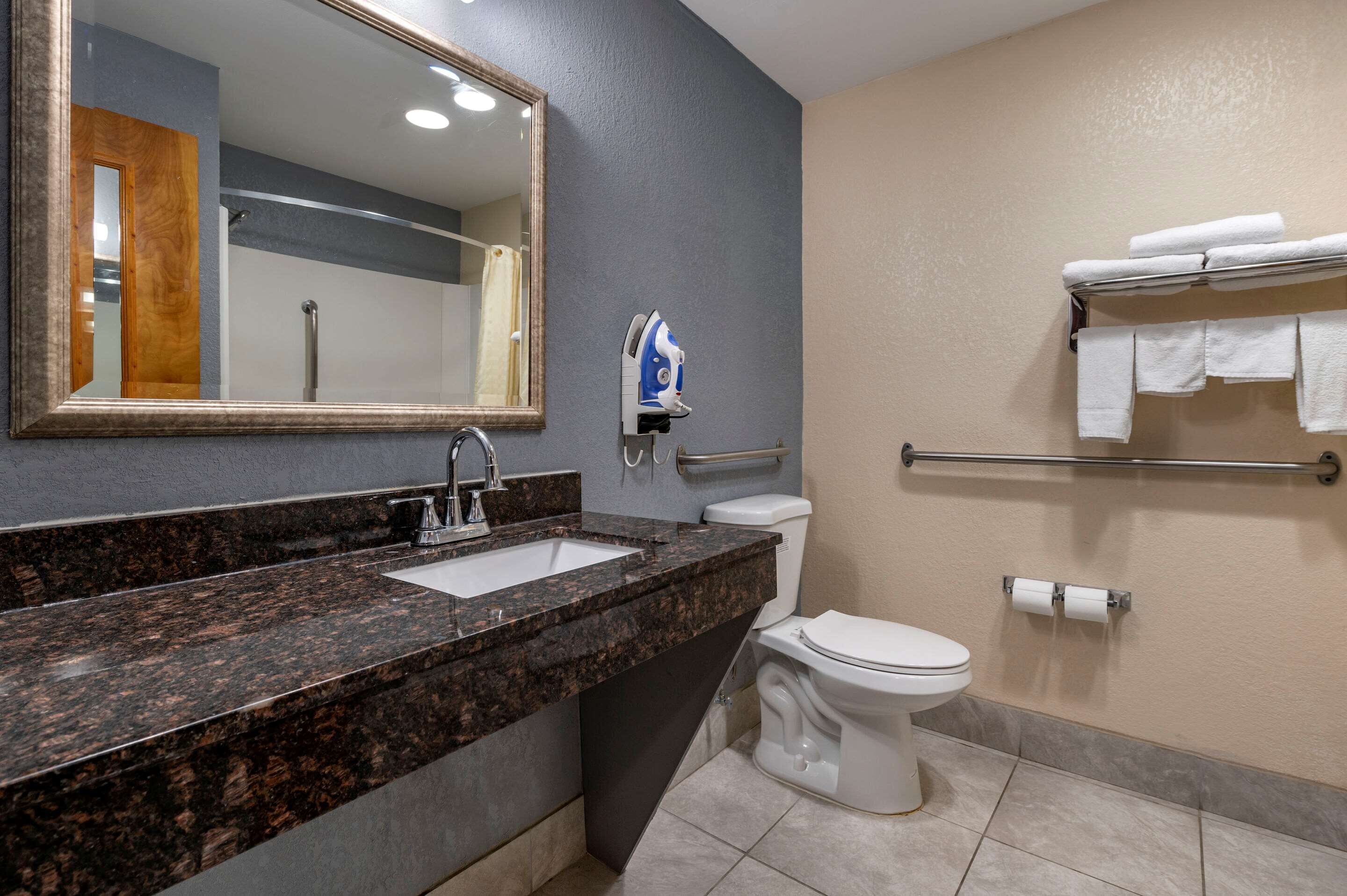 A bathroom with a granite countertop sink, a toilet, a towel rack, and a mirror.