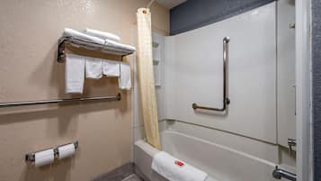 A bathroom with a bathtub, a shower, and a handrail. There are towels and toilet paper on the wall.