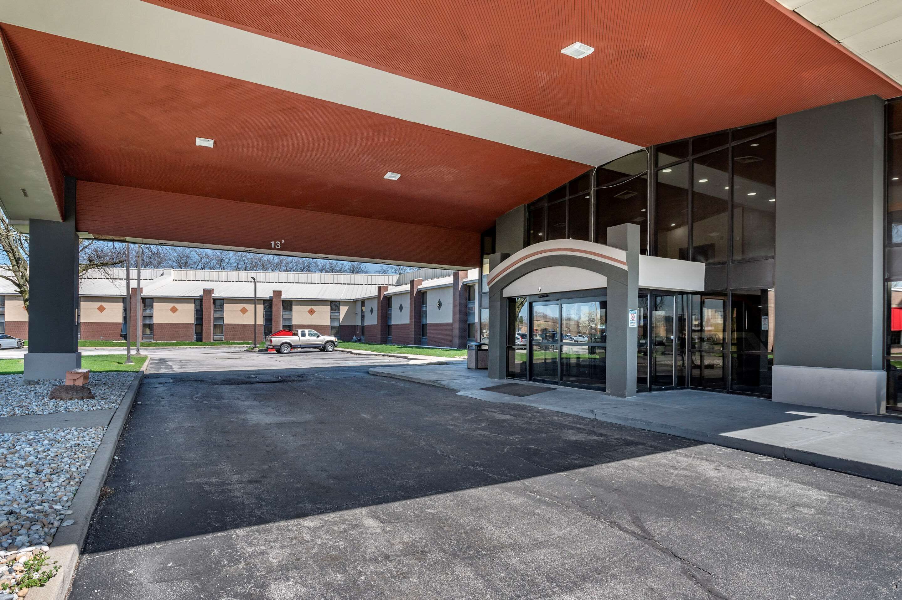 A modern building entrance with a covered walkway, large windows, and a parking area.