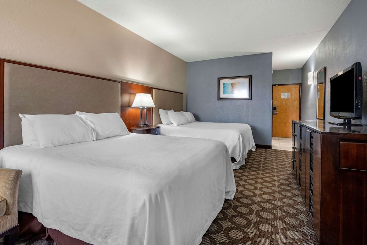 A hotel room with two beds, a desk with a television, a lamp, and a framed picture on the wall.