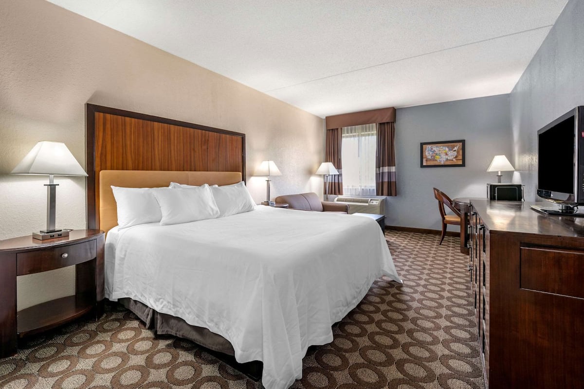 A hotel room with a large bed, two bedside tables with lamps, a desk with a television, and a chair.