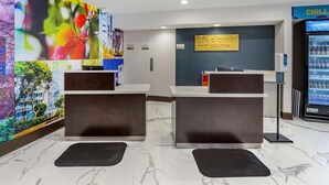 A hotel reception area with marble flooring, a digital screen displaying a cityscape, a reception desk, a 'Chill' beverage machine, and a wall-mounted sign. - Clarion Pointe Raleigh Midtown (Raleigh)