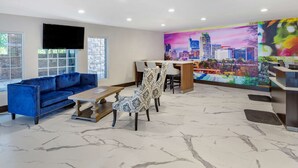 A modern lobby with a blue sofa, a wooden coffee table, patterned chairs, a cityscape mural, and a reception desk. - Clarion Pointe Raleigh Midtown (Raleigh)