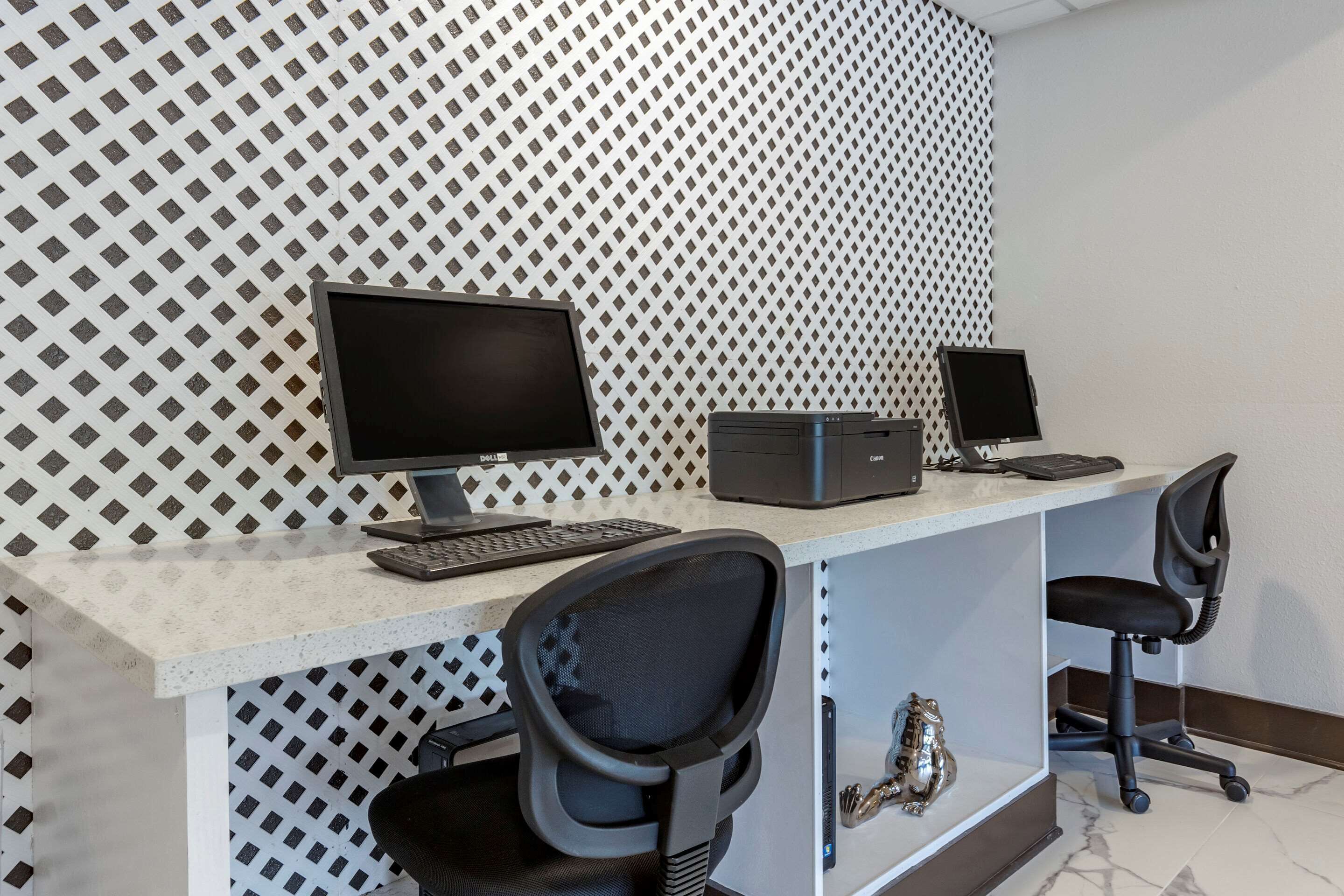 Escritorio moderno con dos monitores, un teclado y un ratón. Hay dos sillas de oficina y un objeto decorativo en la estantería.