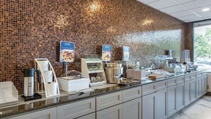 A breakfast bar with a mosaic tile backsplash, a coffee station, and a display of yogurt and cereal options. - Clarion Pointe Raleigh Midtown (Raleigh)