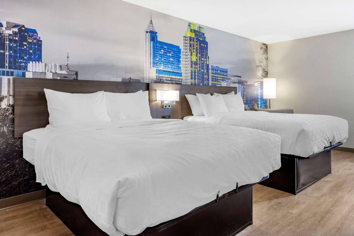 A hotel room with two beds, a cityscape mural on the wall, and a wooden floor.