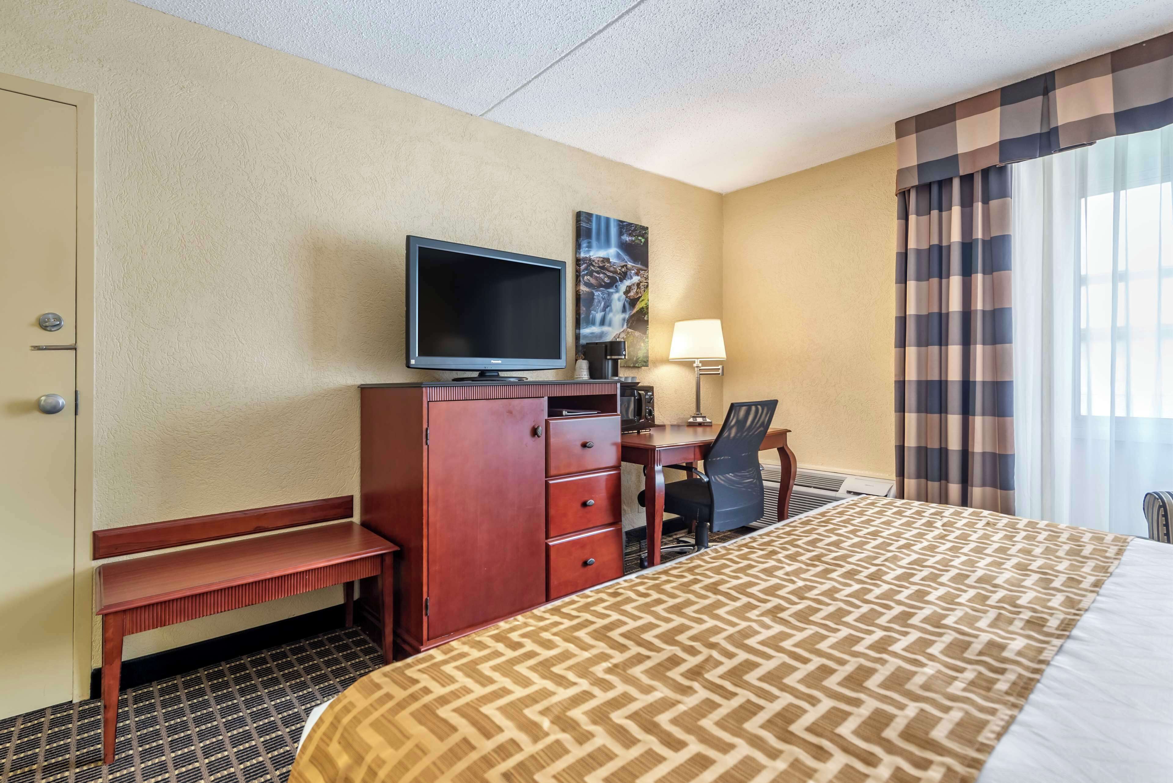 A hotel room with a bed, a desk with a computer, a television, a lamp, and a painting on the wall.