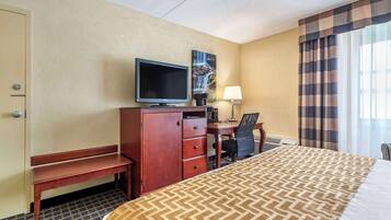 A hotel room with a bed, a desk with a computer, a television, a lamp, and a painting on the wall.