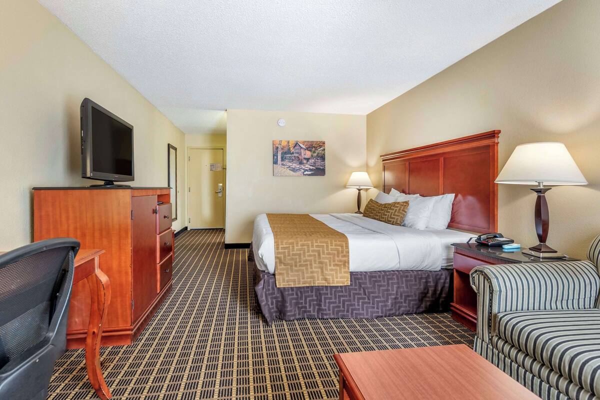 A hotel room with a bed, desk, chair, television, lamps, and a painting on the wall.