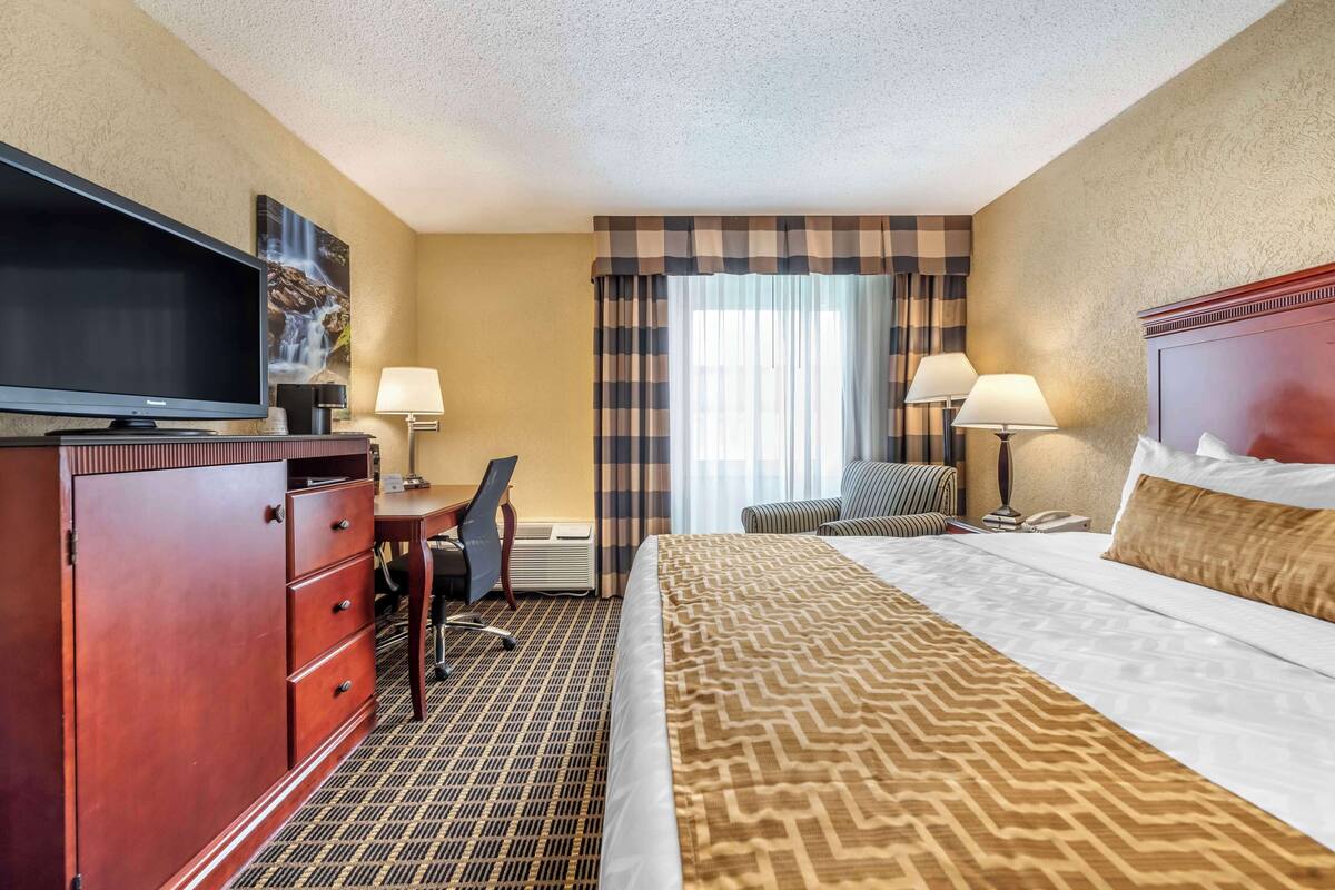 A hotel room with a bed, a desk, a television, two lamps, a chair, and a window with curtains.
