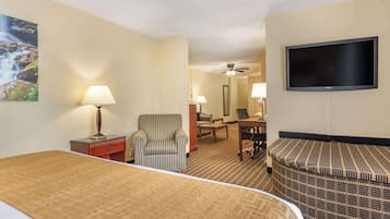 A hotel room with a bed, a striped armchair, a desk with a chair, a television, and a ceiling fan.