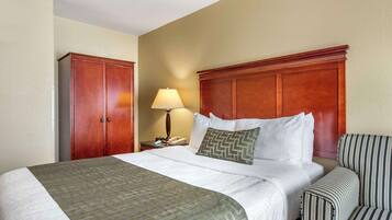 A hotel room with a large bed, a wooden headboard, a bedside table with a lamp, and a striped armchair.