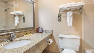 A bathroom with a granite countertop, two sinks, a large mirror, a toilet, and a towel rack with folded towels.