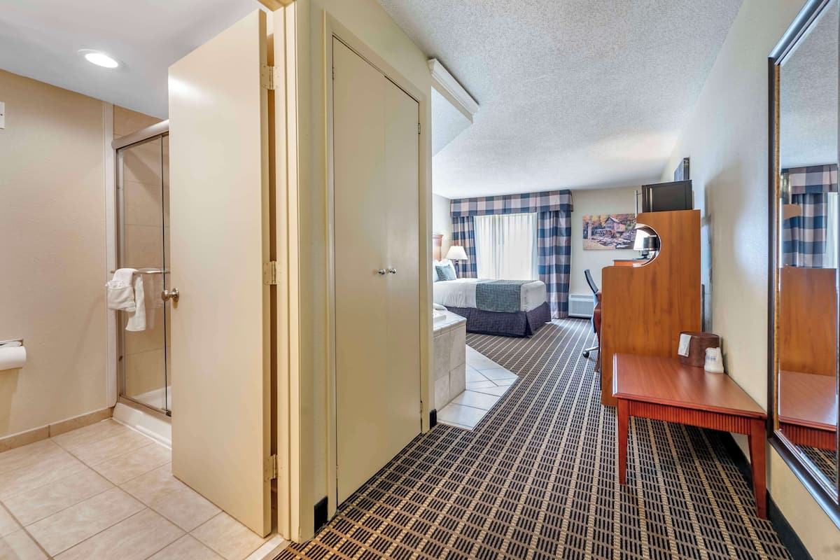 A hotel room with a bathroom, a bed, a small table, and a mirror.