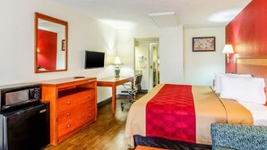 Ein Hotelzimmer mit Bett, Schreibtisch, Stuhl, Fernseher und einer kleinen Küchenzeile.