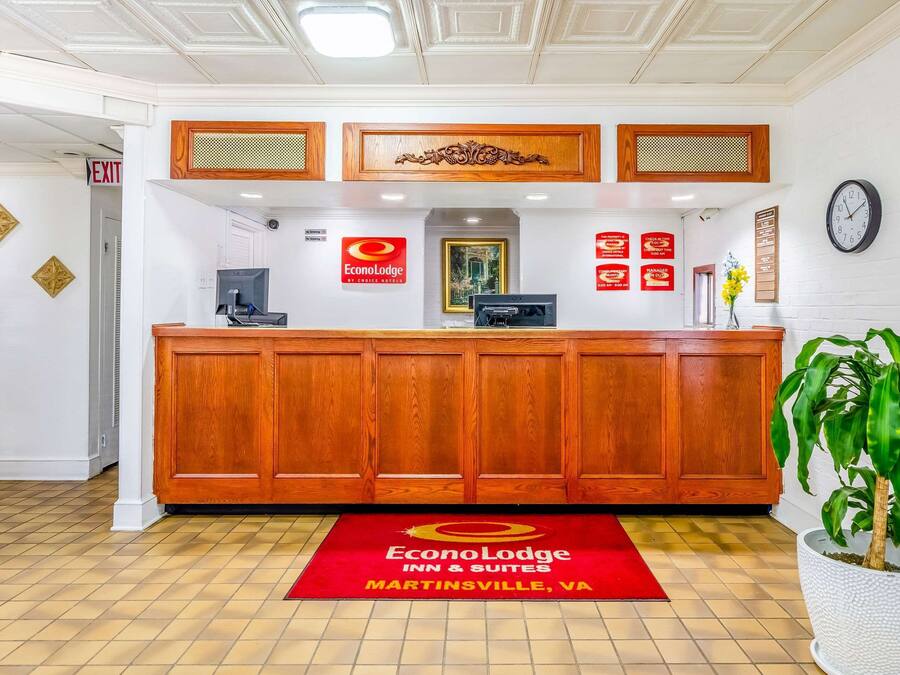 A reception area with a wooden reception desk, a clock, and a red carpet with the hotel name.