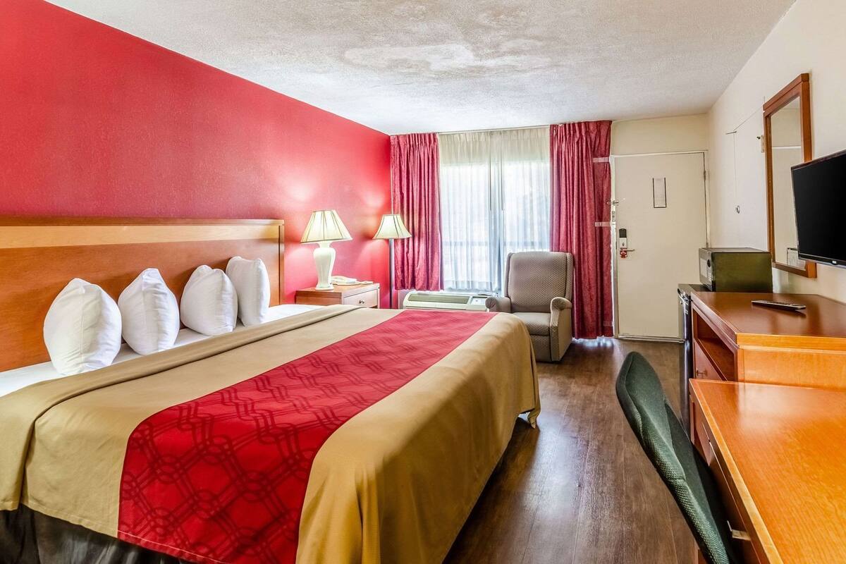 A hotel room with a large bed, a desk, a chair, a television, and a window with curtains.