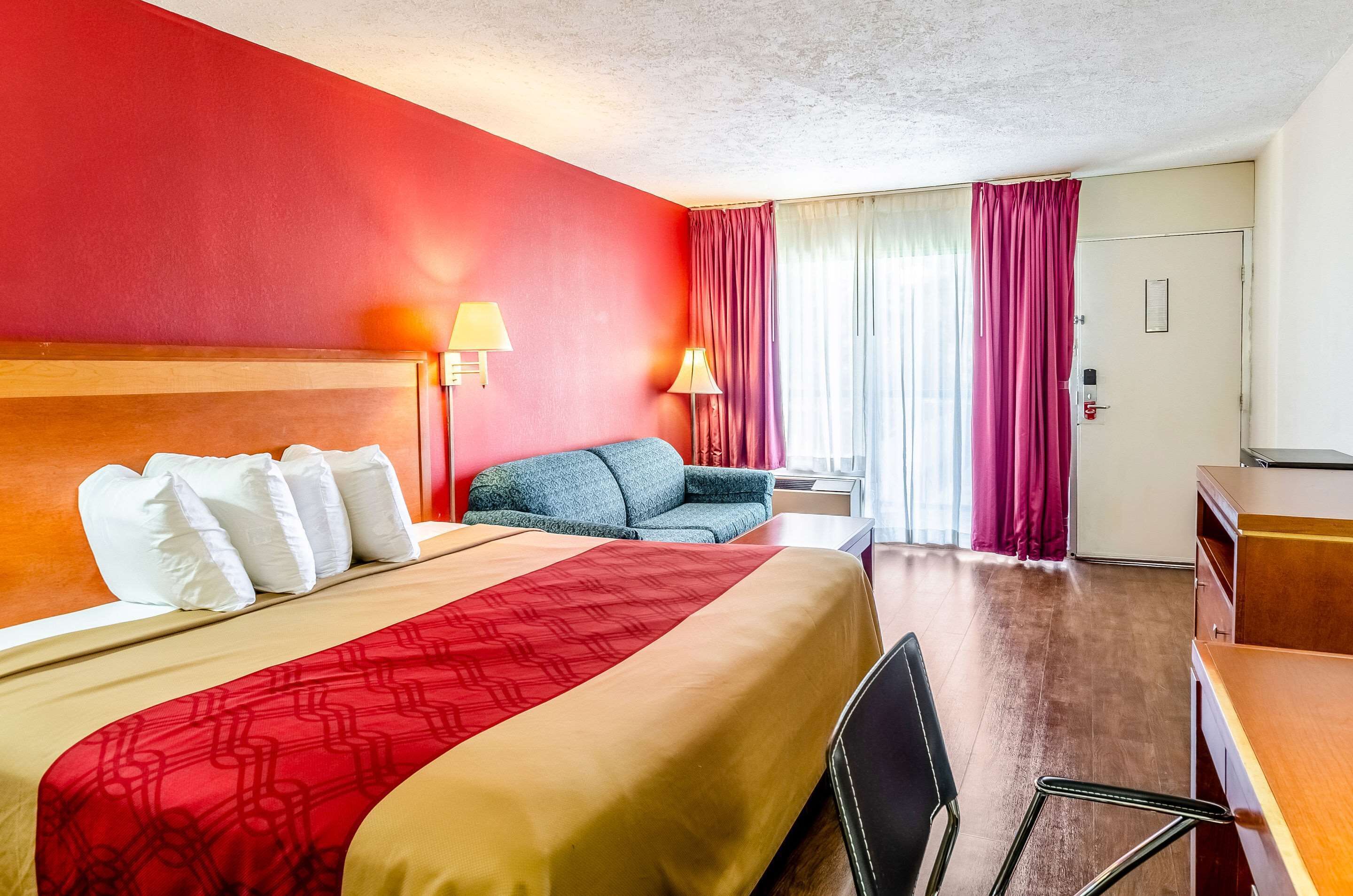 Een hotelkamer met een groot bed, een bureau, een stoel, een bank en een raam met gordijnen.