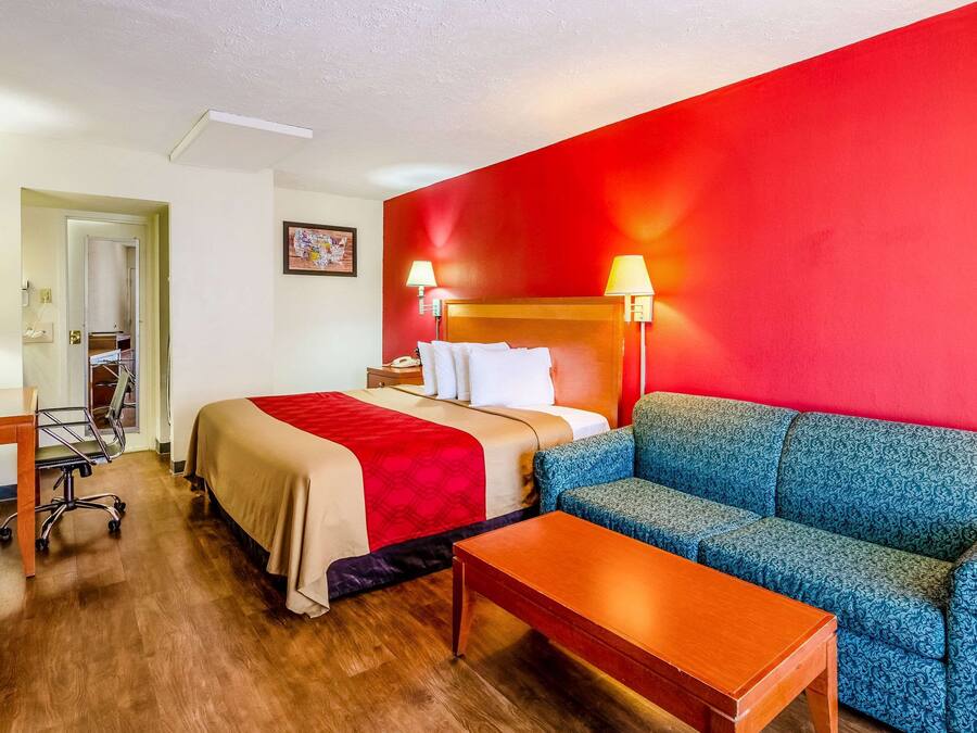 A hotel room with a bed, a blue sofa, a wooden table, and a desk with a chair.