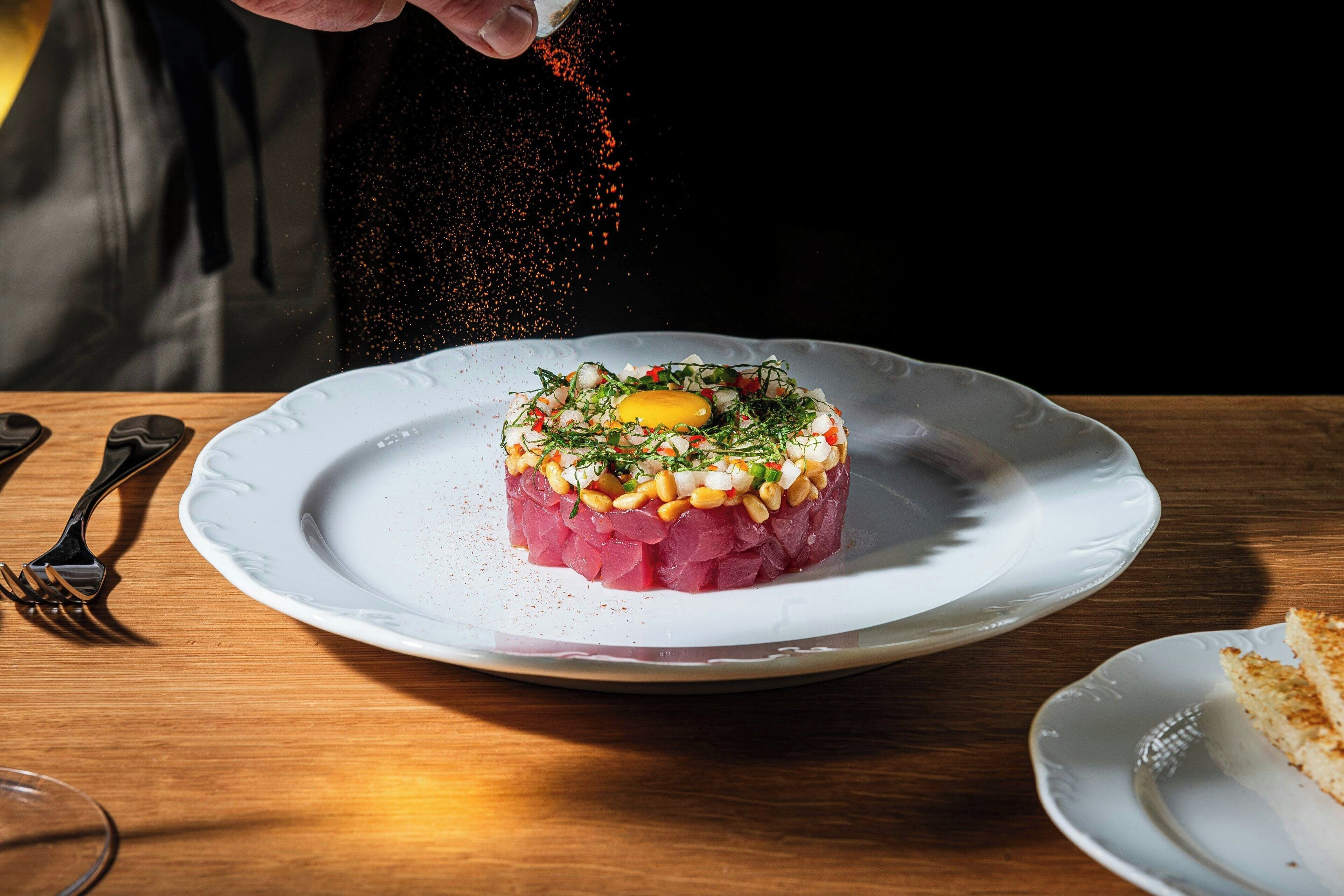 Un plato de tártara de carne con yema de huevo cruda, decorado con hierbas y nueces, sobre un plato blanco.