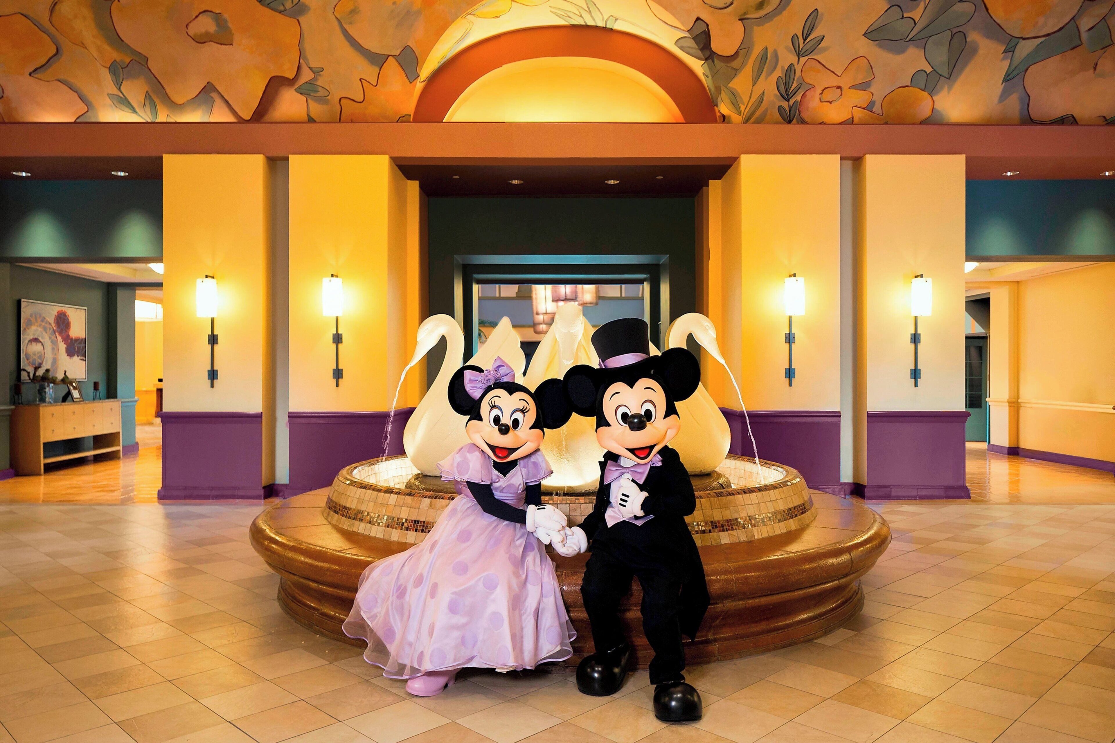 Mickey and Minnie Mouse standing in front of a fountain with a floral ceiling and wall sconces.