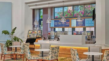 A hotel lobby with seating areas, a reception desk, and a window with a view of pink flowers.