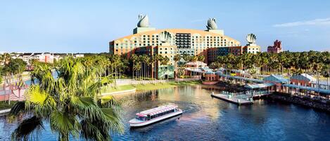 A large hotel with a distinctive architectural design featuring swan-shaped elements on the roof, situated by a body of water with a boat docked nearby.