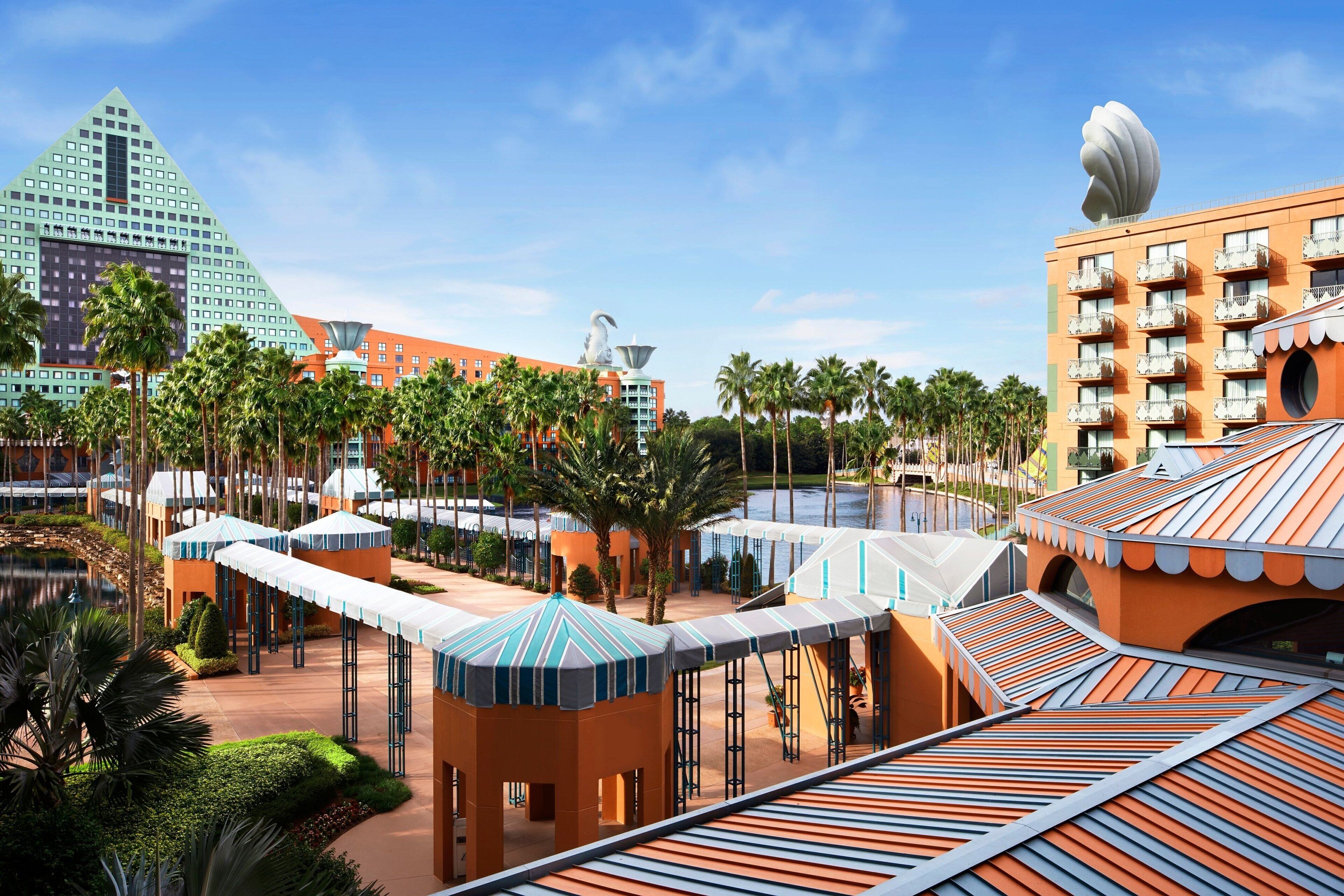 Un resort con un grande edificio dalla forma distintiva a piramide, una superficie d'acqua e una spiaggia attrezzata con ombrelloni e palme.