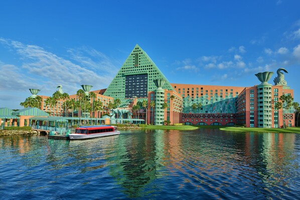 A hotel with a pyramid-shaped building, a boat on the water, and palm trees. - Walt Disney World Dolphin (Lake Buena Vista)