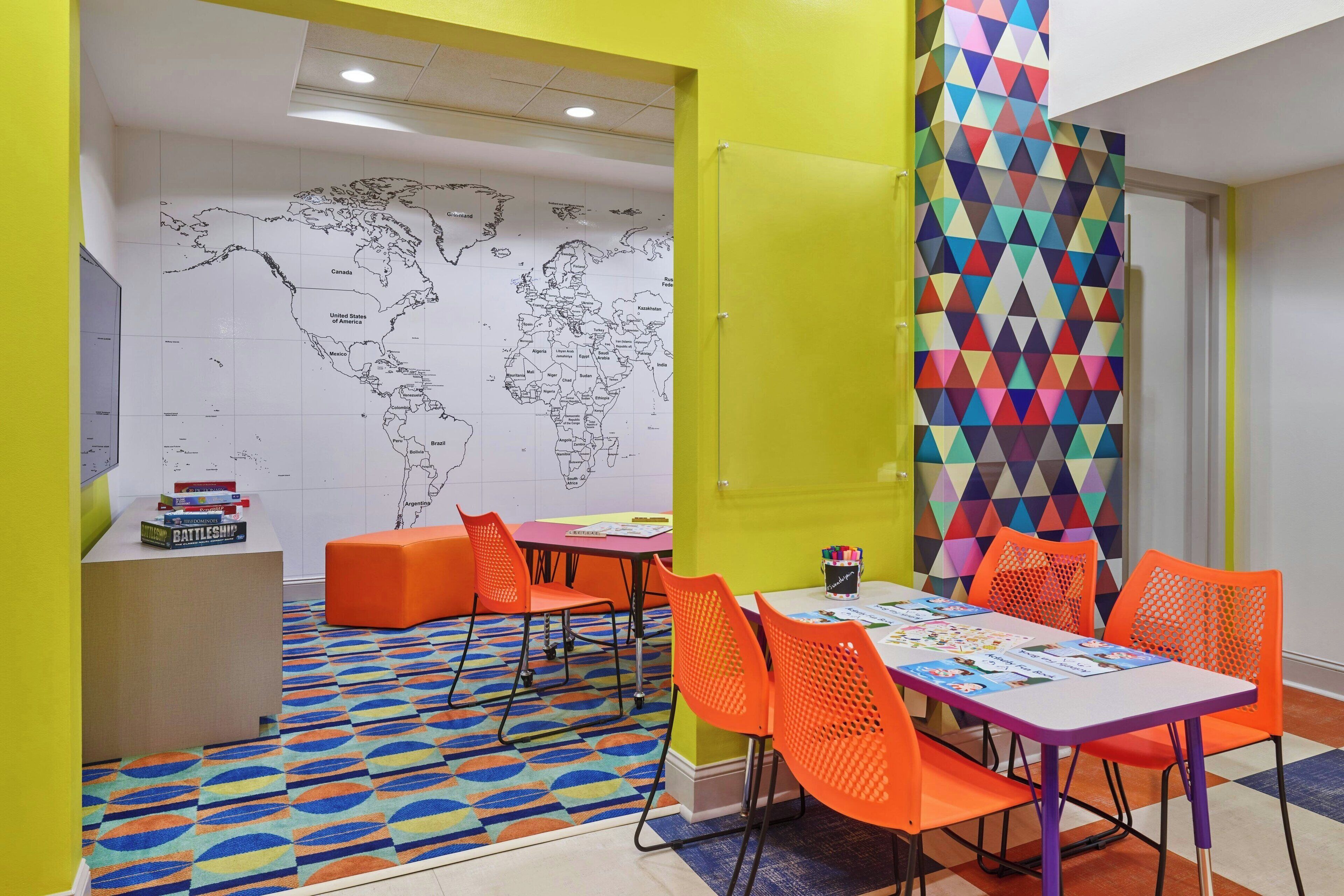 A brightly colored room with a world map on the wall, orange seating, and a colorful geometric wall panel.