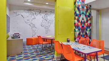 Una habitación de colores vivos con un mapa mundial en la pared, asientos naranjas y un panel de pared geométrico y colorido.