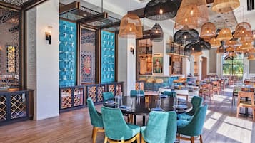A spacious dining area with round tables and teal chairs, surrounded by decorative woven light fixtures.