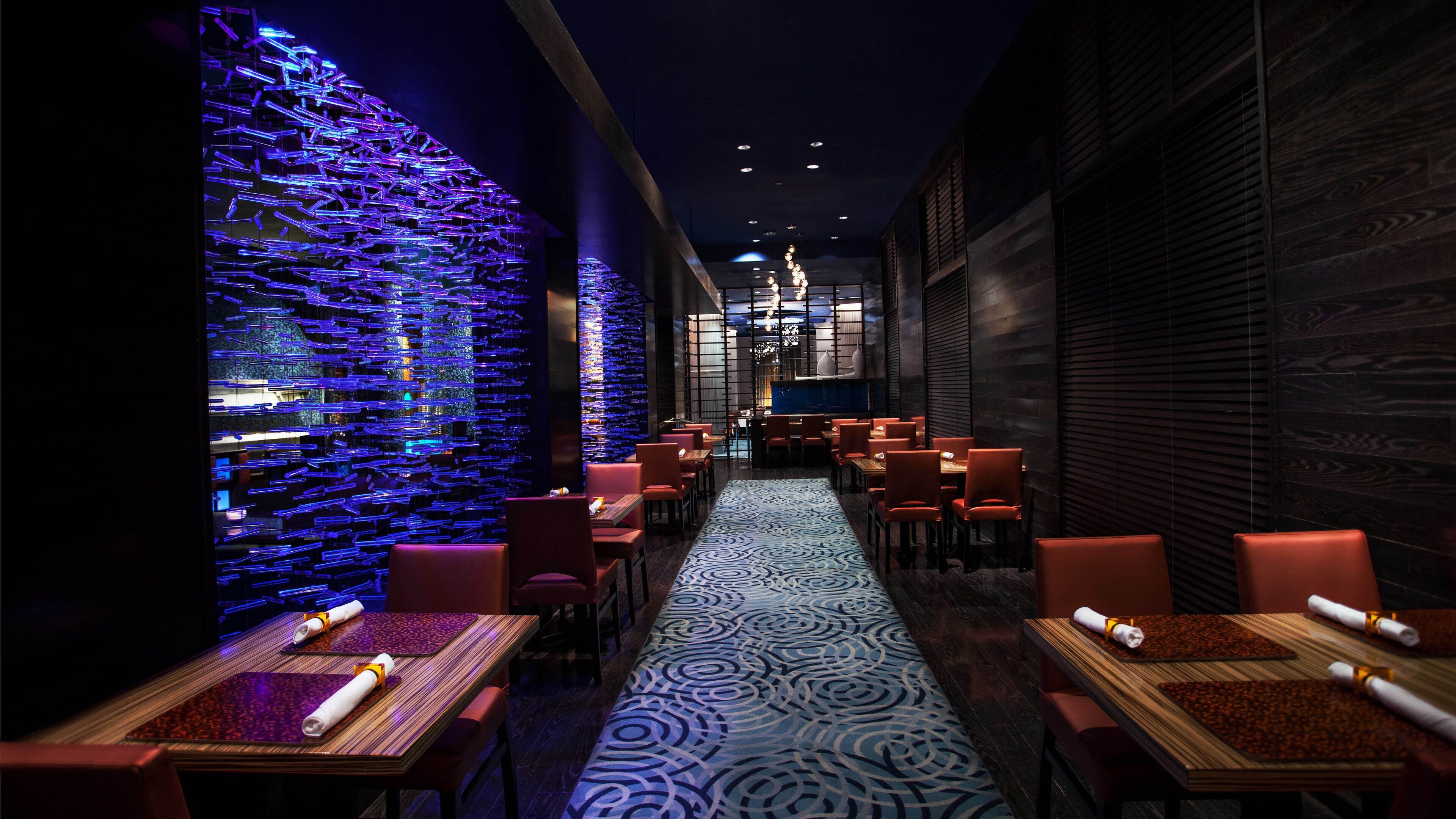 A restaurant with a modern interior, featuring a patterned floor, red chairs, and tables with napkins.