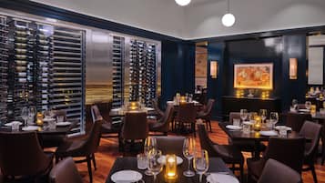 A restaurant with multiple dining tables set with candles, wine bottles, and glasses.