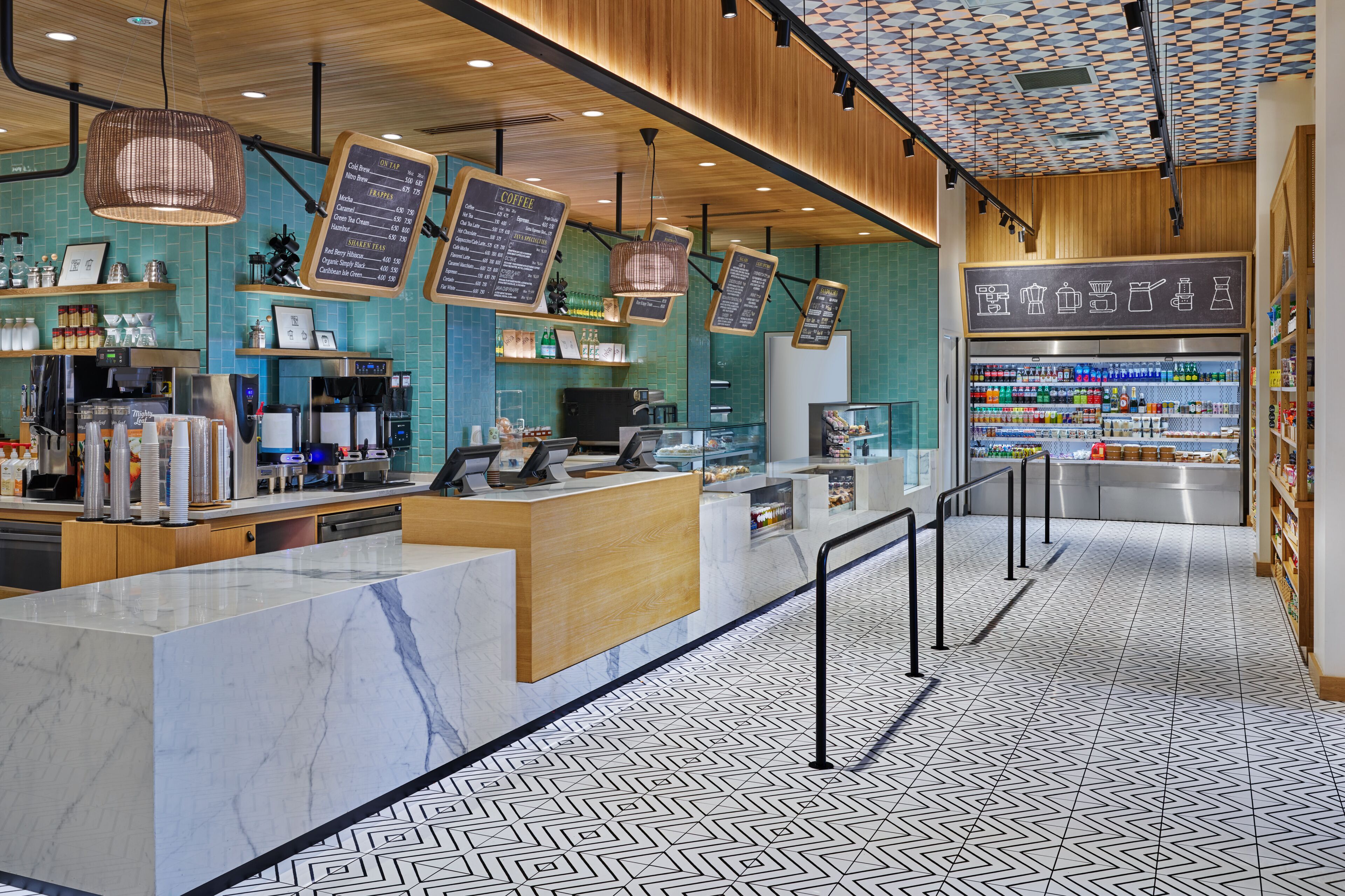 Un interior de cafetería moderna con mostrador de mármol, lámparas colgantes y suelo con estampado.