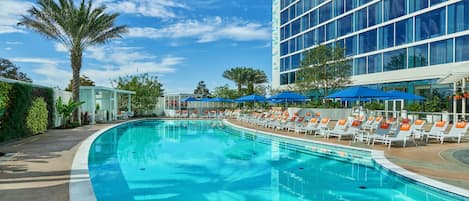 A swimming pool with lounge chairs and umbrellas, surrounded by a building with large windows.