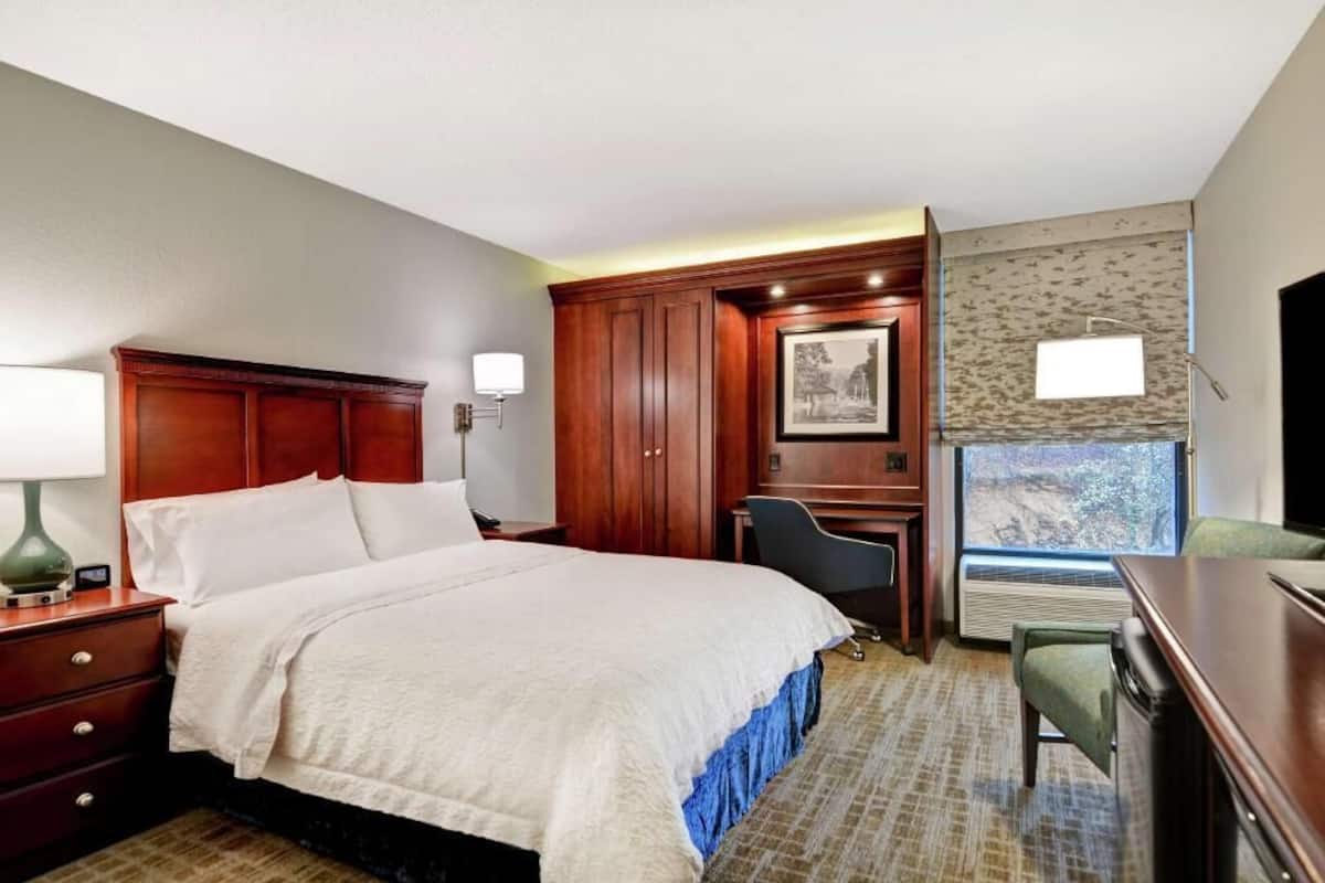 A hotel room with a bed, desk, chair, and a large window with a view.