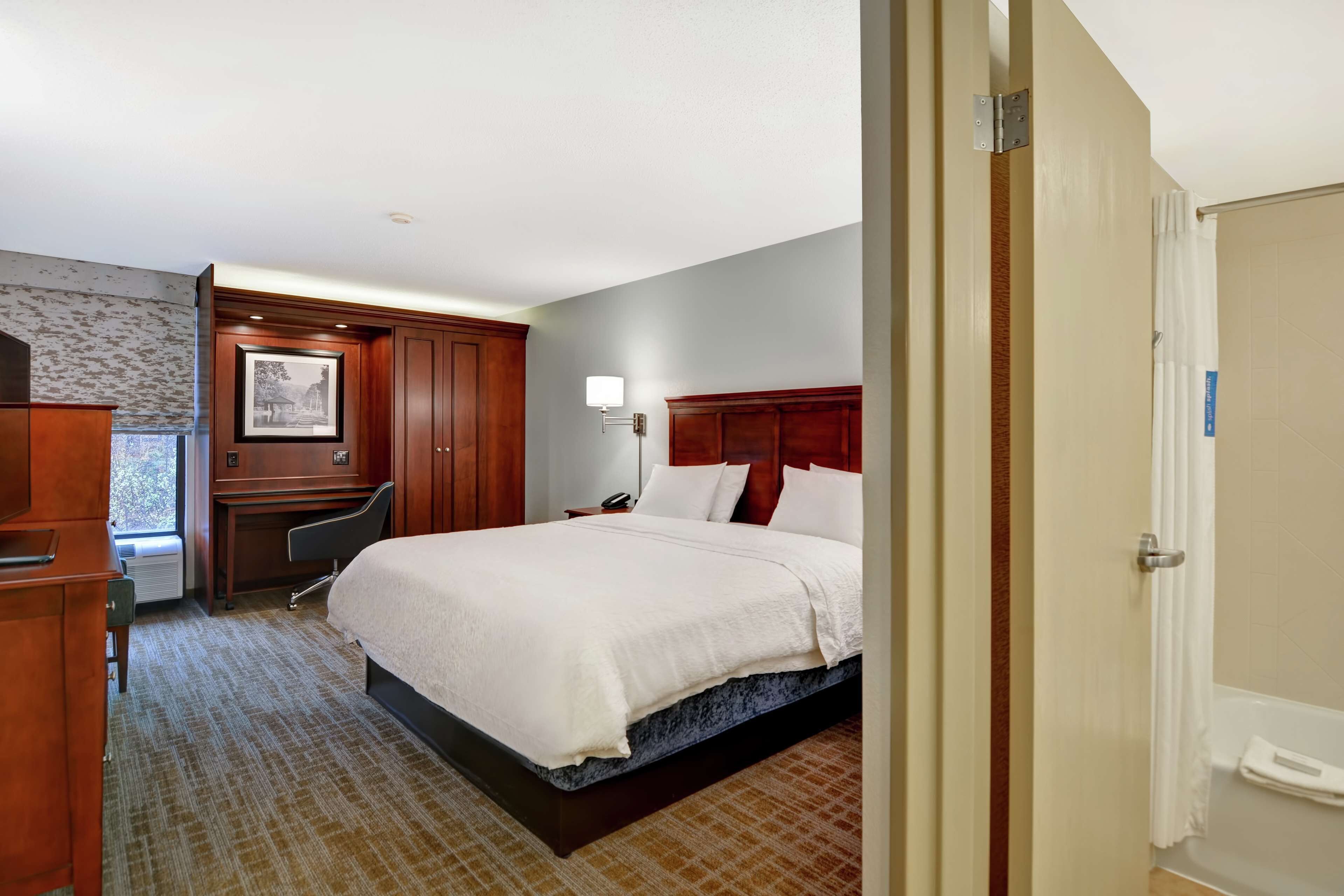 A hotel room with a large bed, a desk, a chair, a desk lamp, and a picture on the wall.