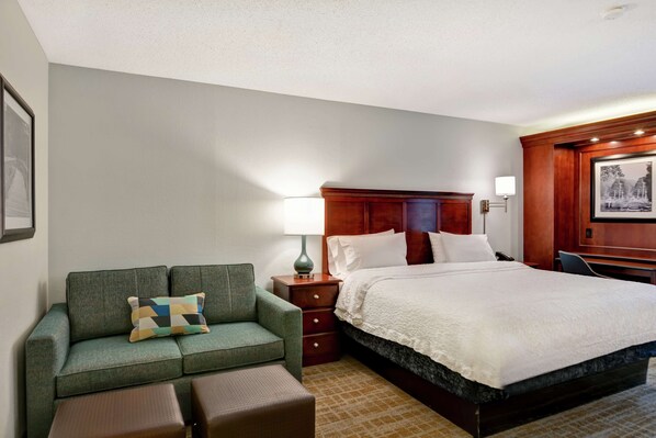 Una habitación de hotel con una cama, un sofá verde, una mesita, una mesita de noche y una lámpara.