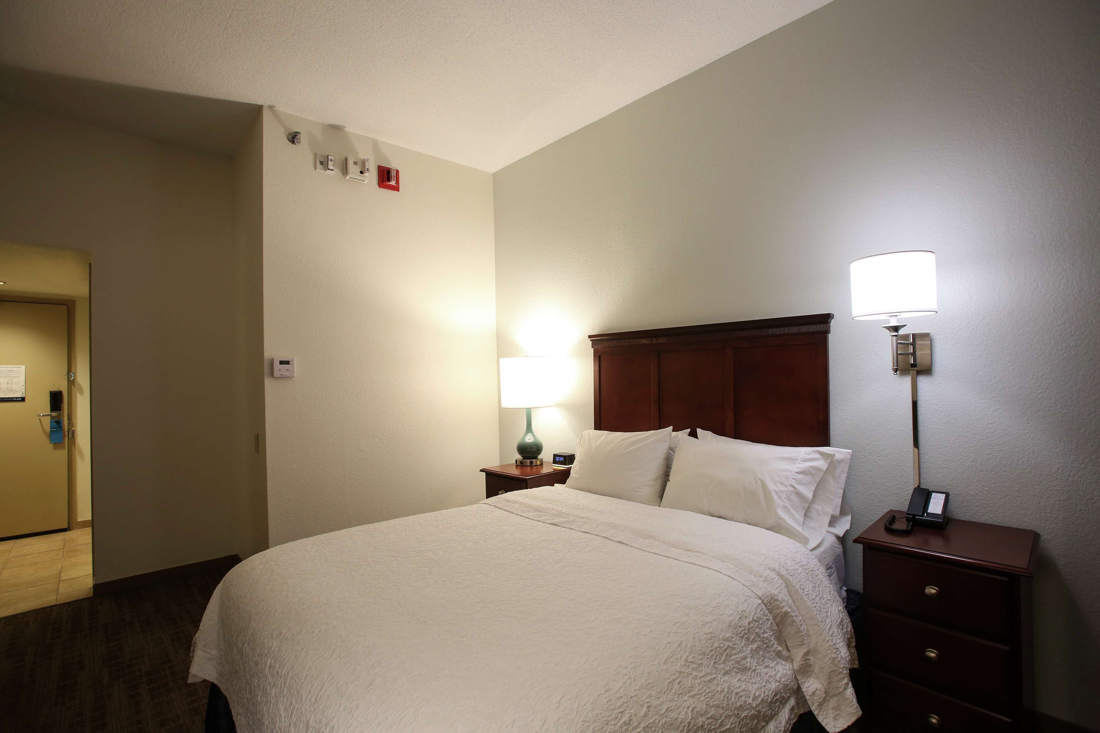 A hotel room with a bed, a nightstand with a lamp, a wooden headboard, and a door with a sign.
