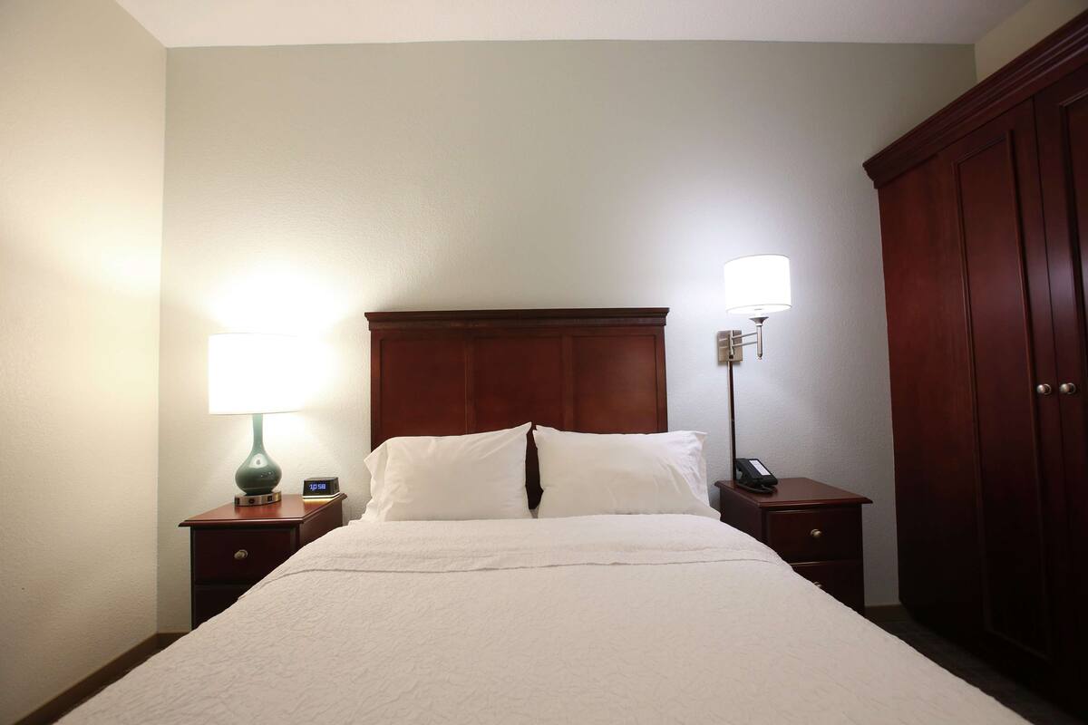 A neatly made bed with a white comforter and pillows, flanked by two bedside tables with lamps and a clock.