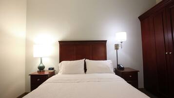 A neatly made bed with a white comforter and pillows, flanked by two bedside tables with lamps and a clock.