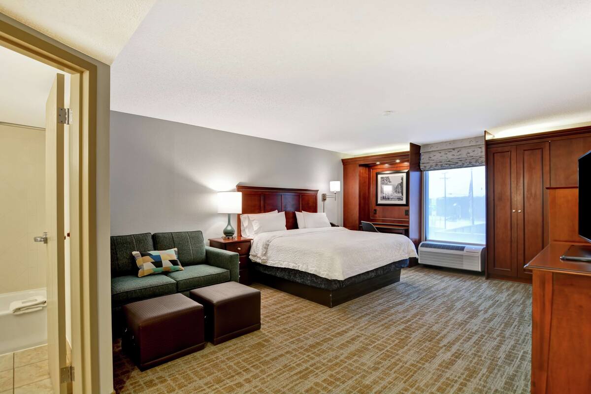 A hotel room with a bed, a sofa, a desk, and a window.